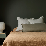 Bed with brown bedding and striped pillows against a dark wall, with a side table and lamp.