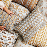 Patterned pillows on a surface with a hand reaching towards one of them.