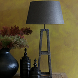 Table lamp with a dark gray shade on a wooden stand against a mustard yellow wall.