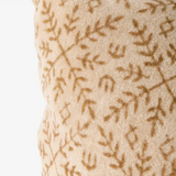 Close-up of a textured woven fabric in warm beige with a repeating brown leafy branch pattern, shown against a plain white background.